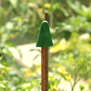 A green rubber cane topper placed on top of a bamboo cane in the garden for eye protection with blurred background