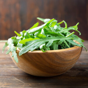 A wooden bowl of freshly picked Cultivated Rocket Arugula green salad leaves.