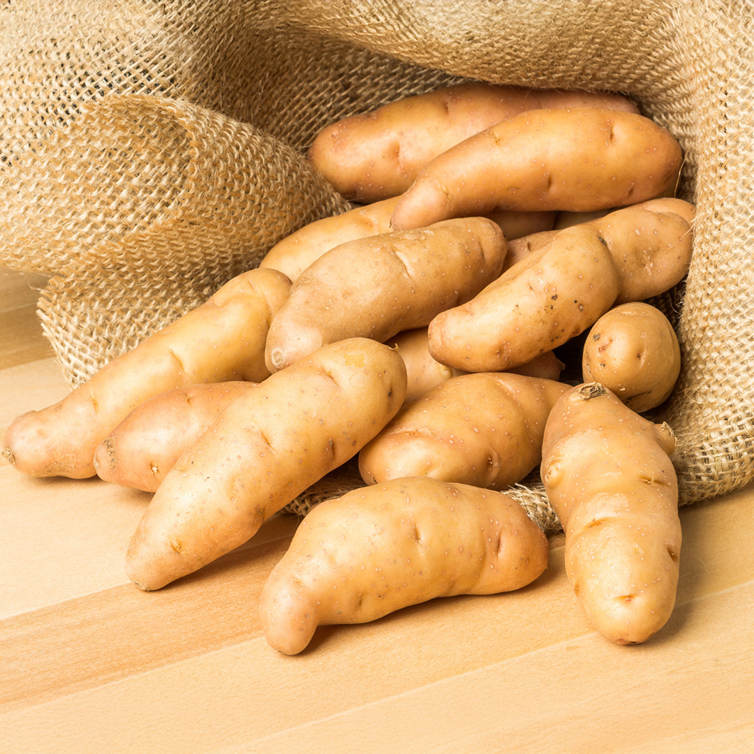 Anya salad fingerling potatoes spilling out of a burlap sack onto a wooden table.