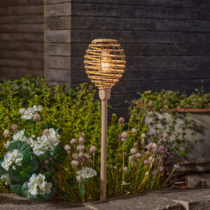Faux rattan solar powered stake light in a garden with flowers behind