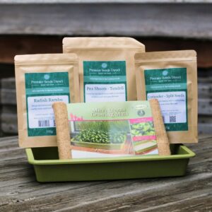 a green seed tray with hemp growing mats and three packets of microgreens seeds on display on a bench top