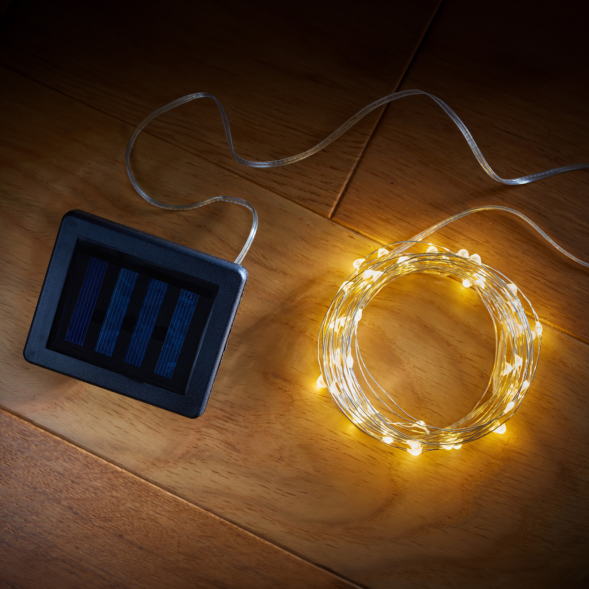 A reel of solar powered LED metal string lights rolled up with the charger on a wooden table