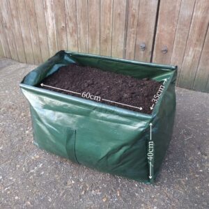 A rectangular green growing bag filled with compost in front of wooden garden fencing