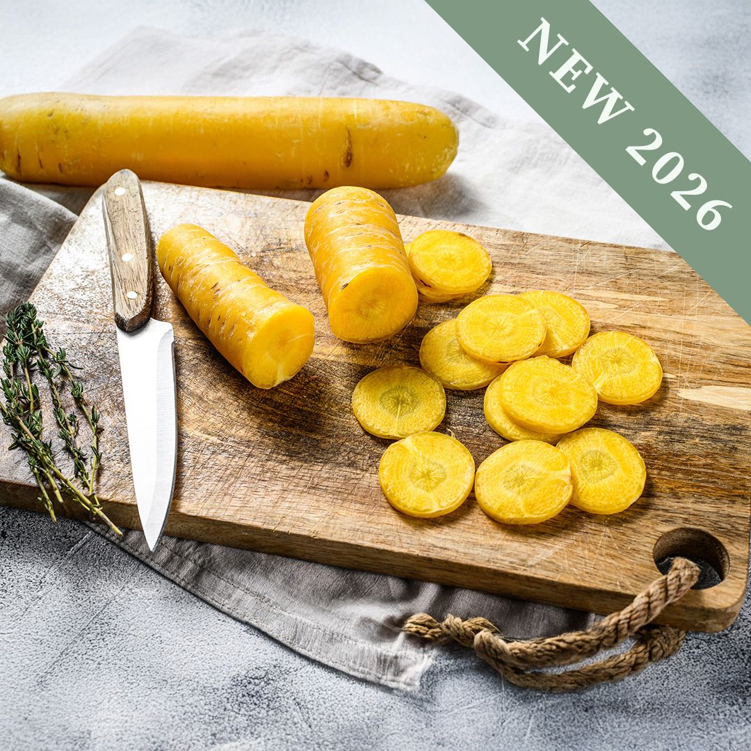 Sliced Yellow Moon Carrots on a wooden chopping board with a sharp knife and herbs on a cloth.