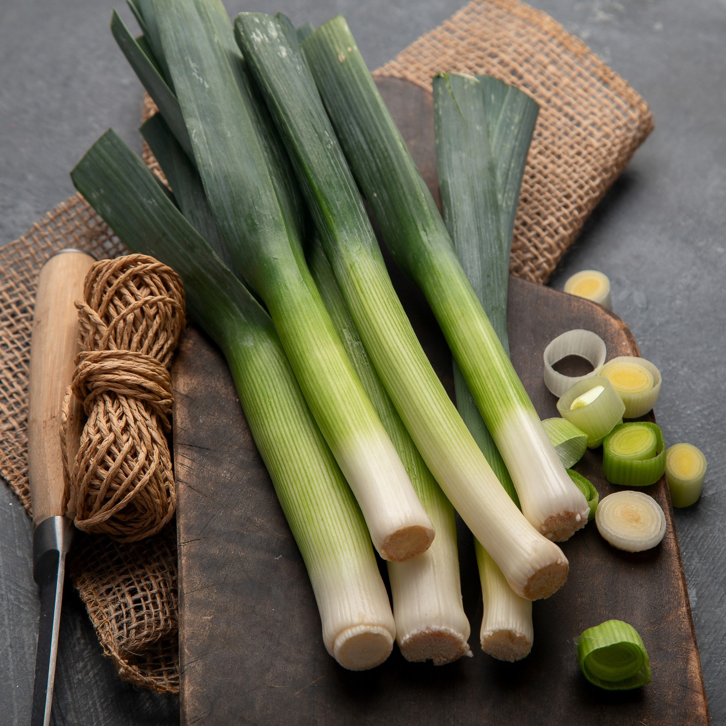 Harvested and sliced Norwich Leeks with green leaves on a wooden board and burlap.