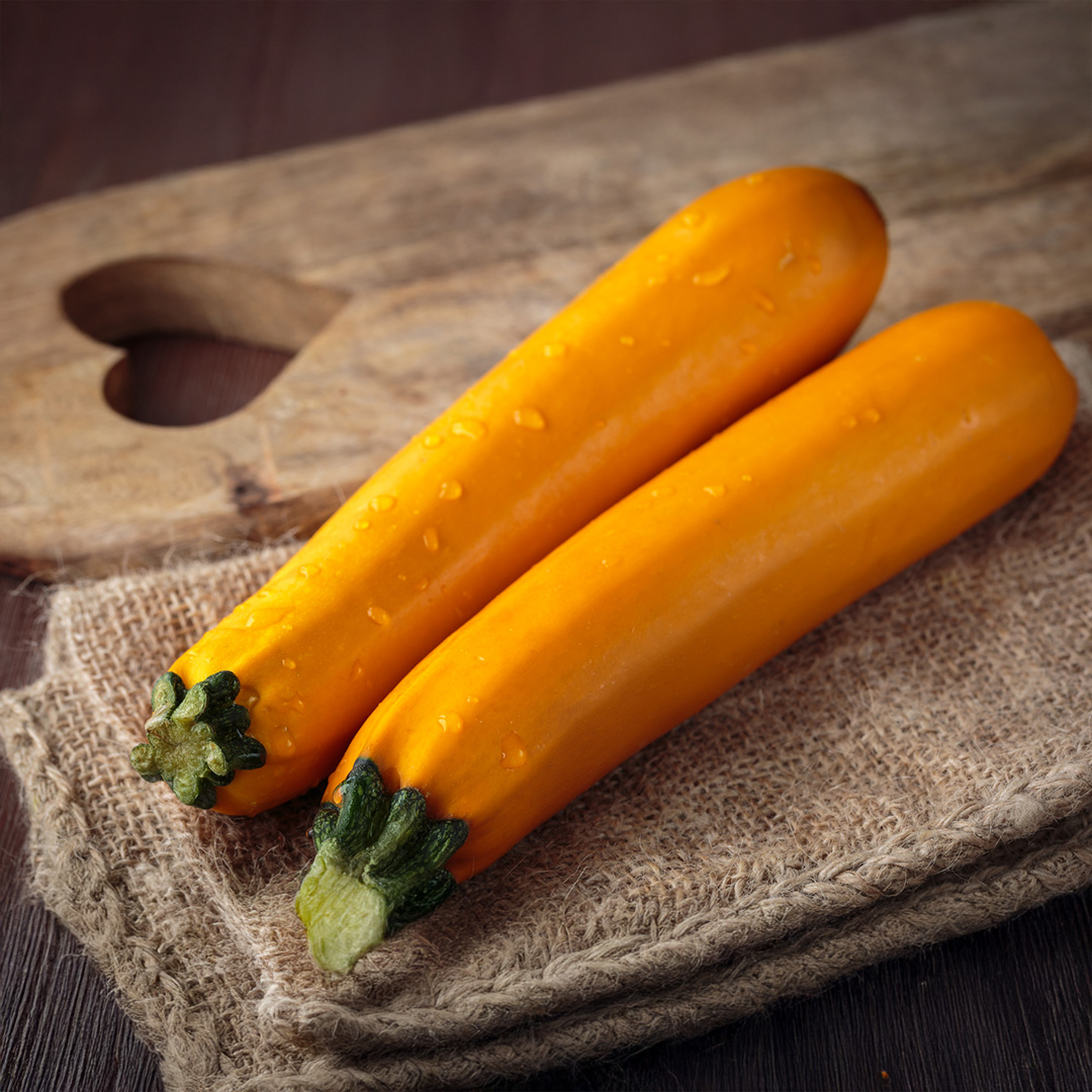 A pair of yellow Sebring Courgette zucchini on burlap next to a wooden chopping board with heart-shaped detail.