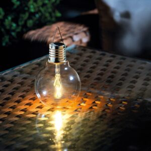 A vintage style solar powered light bulb with filament lit in the night on a table in the garden