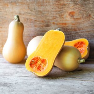 Butternut Waltham Squash freshly harvested on a wooden surface with one sliced open and orange flesh exposed